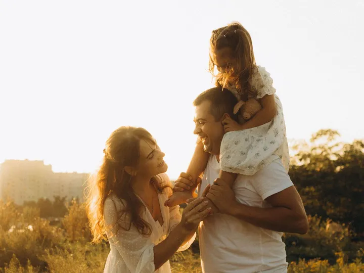 A father and daughter laughing together outdoors with the family at sunset